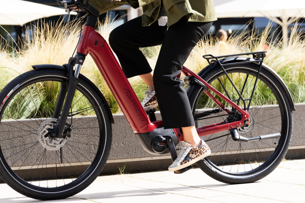 photo taken from the waist down of a person riding a step through ebike, wearing a jacket and leopard print sneakers