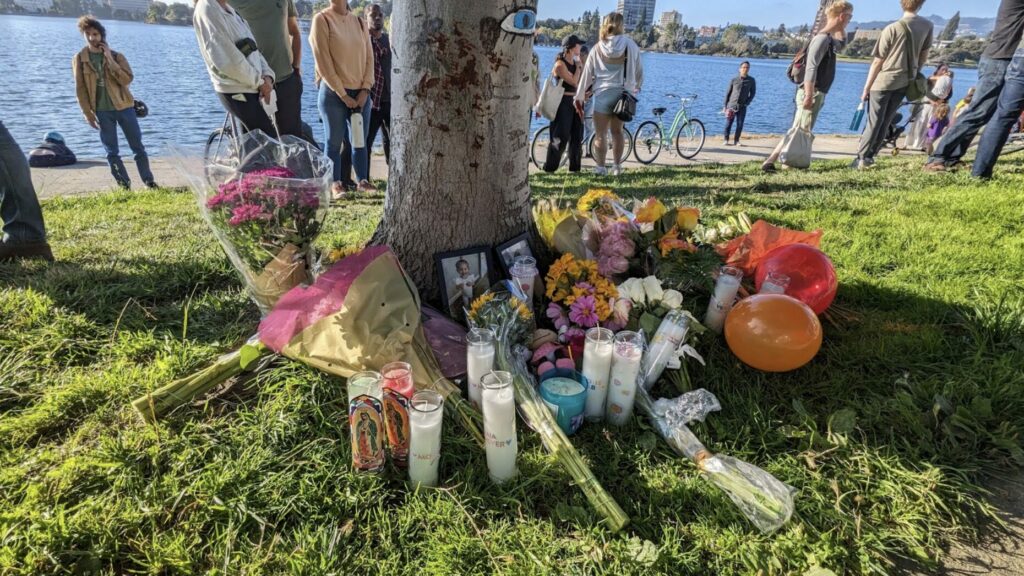 photo of a memorial with flowers photos and candles around a tree at Lake Merritt in Oakland