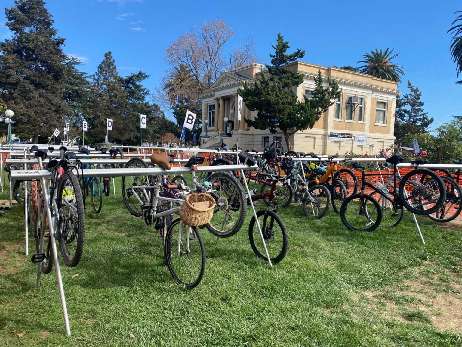 Dozens of bikes hang on racks at Bike East Bay's bike valet program being held in a grassy park.